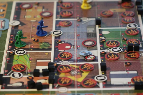 Een coöperatief bordspel met kleine plastic figuurtjes van brandweerlieden op een spelbord vol met vuurfiches.